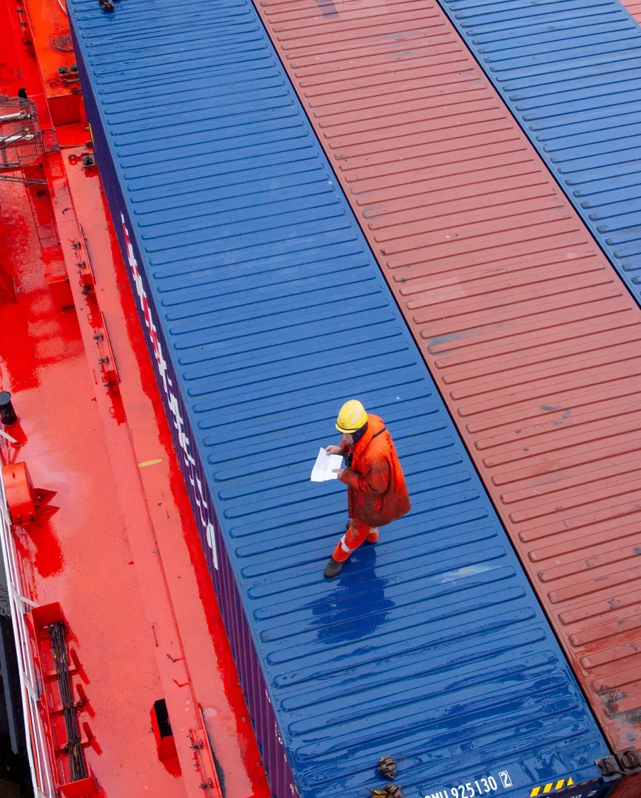 A dock worker in high-visibility gear checking shipping containers during loading