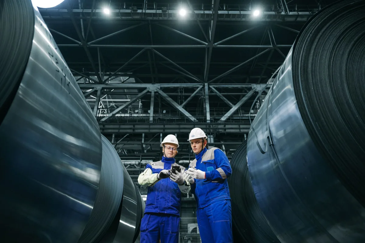 Industrial workers inspecting large steel coils on a factory floor