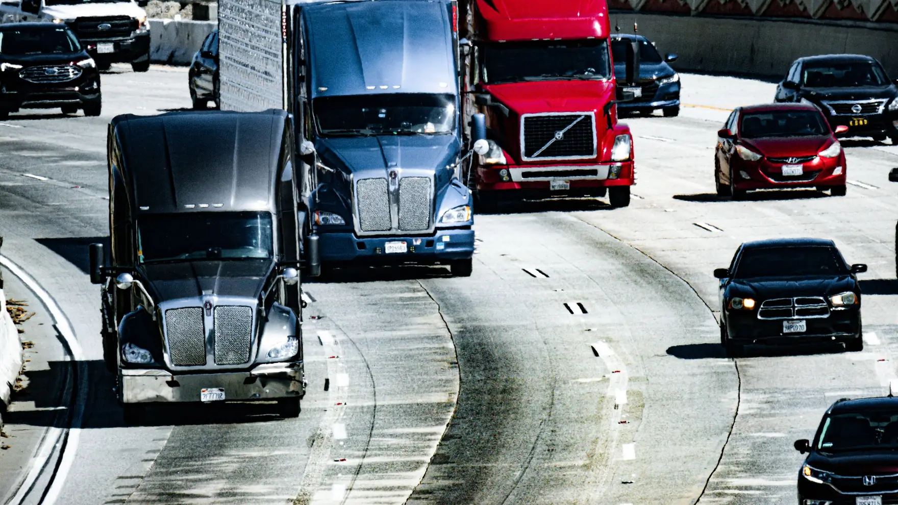 Freight trucks and cars traveling on a multi-lane city highway during daytime under an overcast sky.
