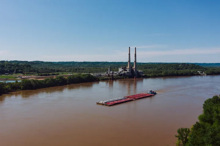 A river barge loaded with shipping containers moving along a calm river under open sky.