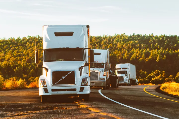 A red Kenworth semi-trailer truck driving down an open highway under a clear blue sky.