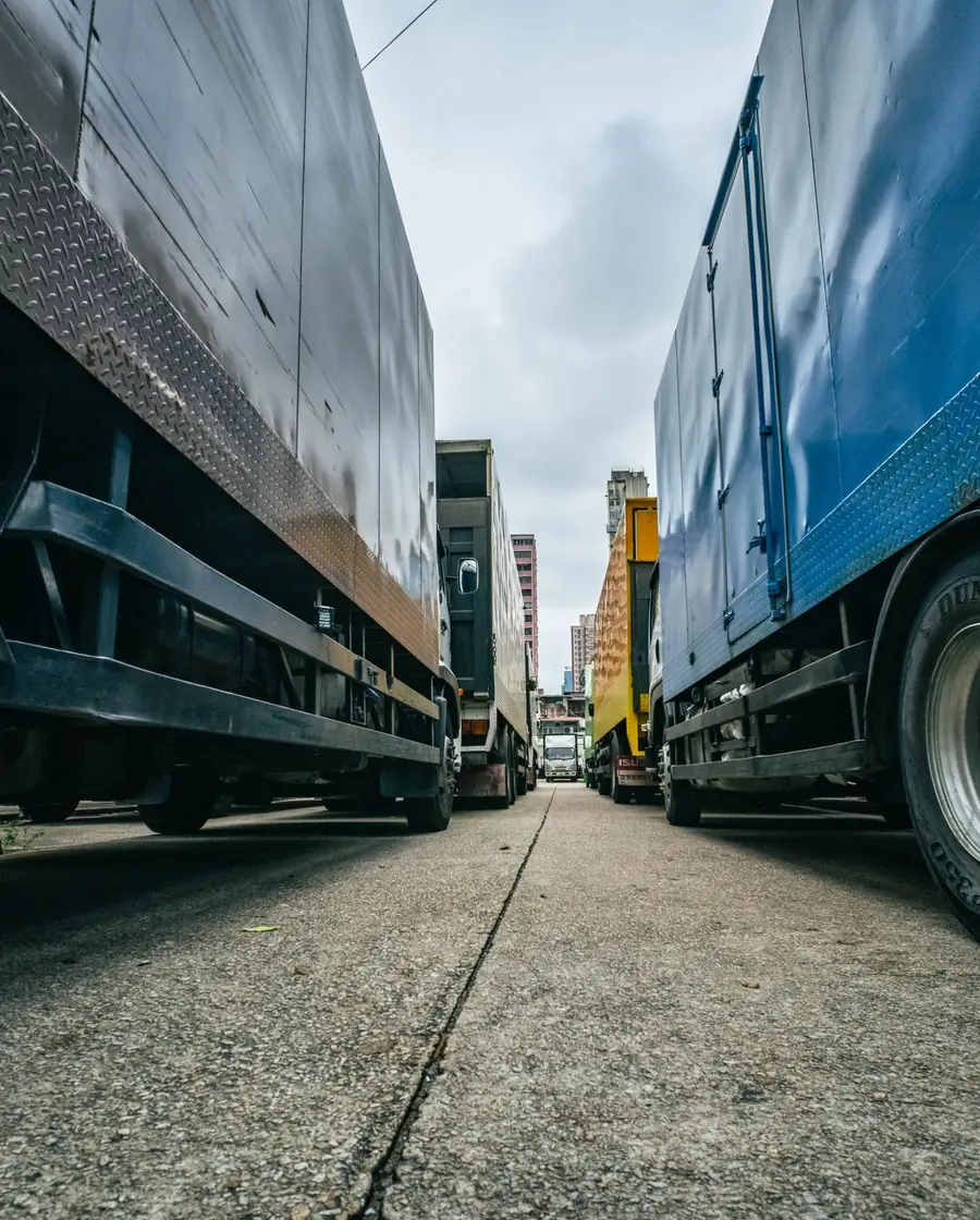 Low-angle view of freight trucks lined up in city traffic, framed tall against surrounding buildings.