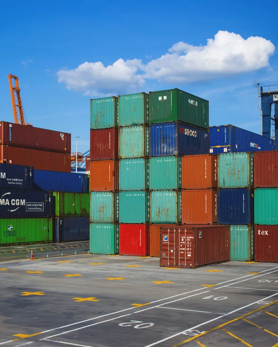 Colorful steel shipping containers stacked several high against a clear blue sky at a terminal.