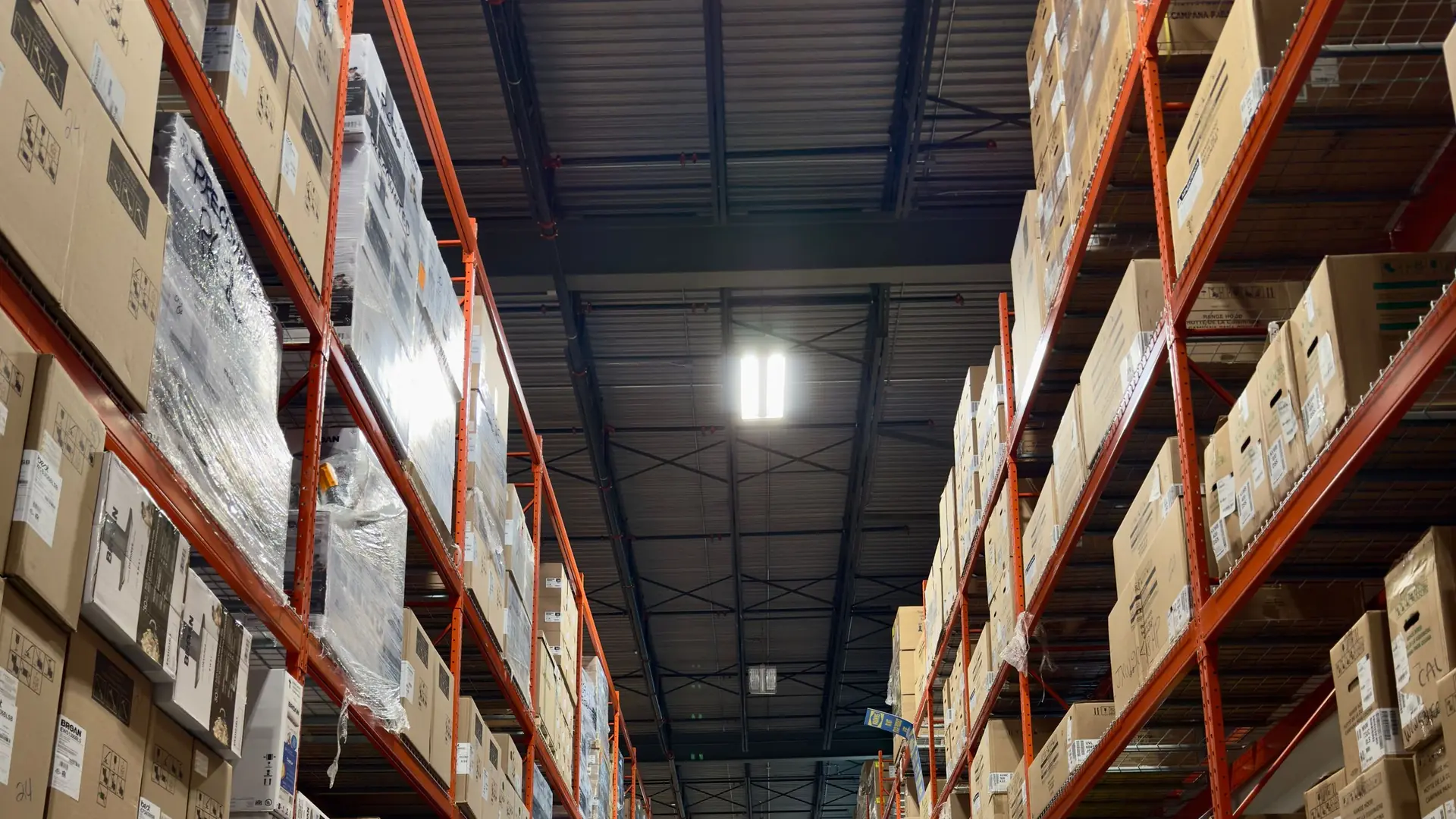 Long warehouse aisle lined with tall racking shelves stacked with boxed products and pallets